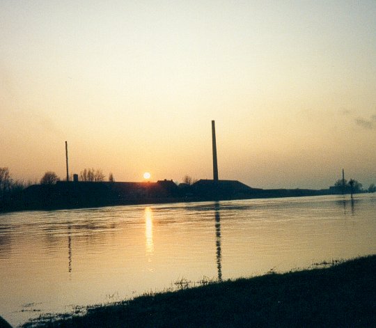 Steenfabriek aan de overkant van de Rijn bij Juffierswaard bij ondergaande zon, die in het water weerspiegelt.